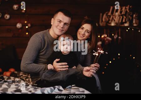 Mignon jeune papa de famille, maman et petite fille avec des barboteurs sur le lit avec fond de Noël derrière Banque D'Images