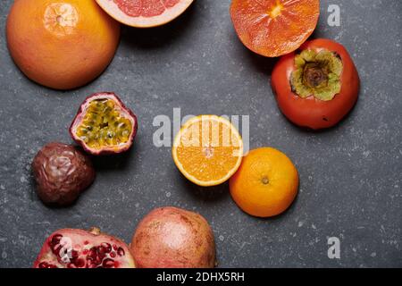 Vue de dessus de l'orange avec pamplemousse, grenade, fruit de la passion et kaki sur fond de pierre gris foncé. Fruits frais et sains pour stimuler la vitamine C. Banque D'Images