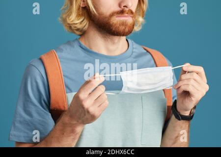 Gros plan d'un jeune homme avec sac à dos derrière son dos masque de protection isolé sur fond bleu Banque D'Images