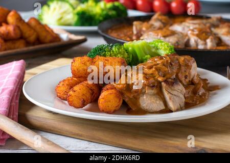 dîner de porc avec filet de porc frit, croquettes et légumes dans une sauce à la crème servie sur une assiette Banque D'Images