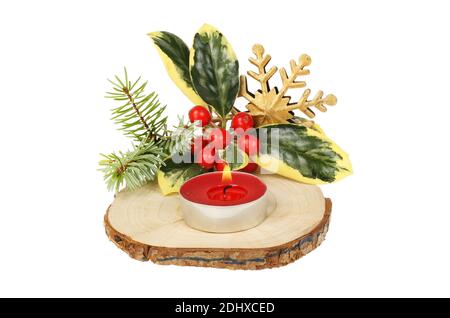 Décoration de table de Noël, bougie brûlante avec houx, aiguilles de pin et étoile de flocon de neige sur une section de rondins isolée contre le blanc Banque D'Images