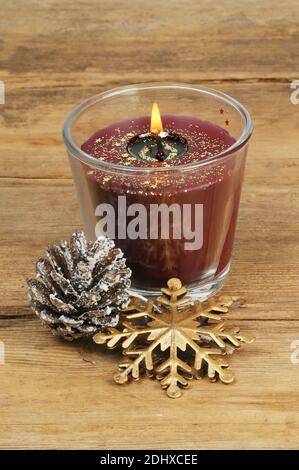 Bougie de Noël éclairée sur bois rustique avec pinecone enneigée et décoration flocon de neige doré Banque D'Images