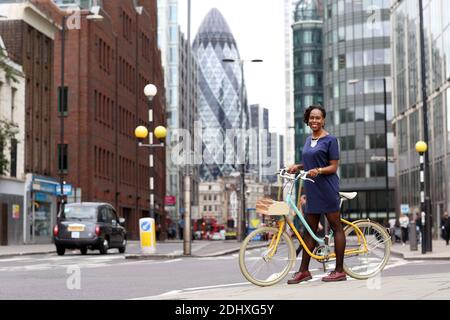 Portrait complet d'une belle femme élégante portant une robe debout avec son vélo à l'extérieur avec la City de Londres en arrière-plan. Banque D'Images