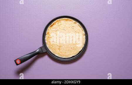 Vue de dessus avec une crêpe française fraîchement cuite dans une poêle en fonte sur un fond violet. Faire des crêpes dans un panoramique, au-dessus de la vue. Banque D'Images