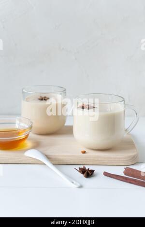 Deux tasses en verre de thé Masala avec épices et miel sur fond blanc. Boisson traditionnelle indienne. Orientation verticale. Copier l'espace. Banque D'Images