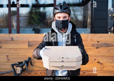 Le préposé à la livraison tient les boîtes à pizza dans une main étirée et se concentre sur le visage. Livraison de nourriture, service de messagerie à vélo au travail, concept de restauration à emporter Banque D'Images