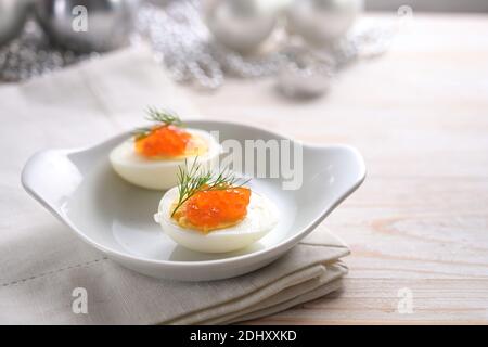 Œufs coupés en deux avec caviar rouge et garniture d'aneth sur une table en bois gris clair avec décoration de Noël, en-cas festif pour une fête de vacances, espace copie, se Banque D'Images