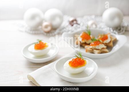 Caviar rouge sur des œufs coupés en deux et des canapés en forme d'étoile, table blanche avec décoration de Noël claire pour un buffet de fête, espace de copie, foyers sélectionnés Banque D'Images