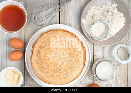 Crêpes sur une assiette plate blanche, œuf, sucre et serviette sur fond clair. Banque D'Images