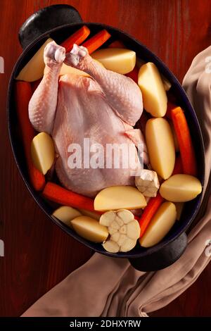 Poulet bio cru entier dans une casserole rustique avec carottes, pommes de terre et ail. Prêt à cuire. Banque D'Images