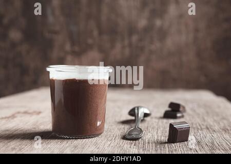 Mousse au chocolat dans un pot en verre, une cuillère à café et des morceaux de chocolat noir sur l'ancienne table Banque D'Images
