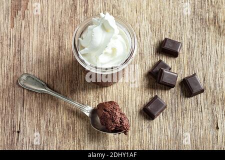 Un verre et une cuillère à café avec mousse au chocolat et morceaux de chocolat noir sur l'ancienne table, vue du dessus Banque D'Images