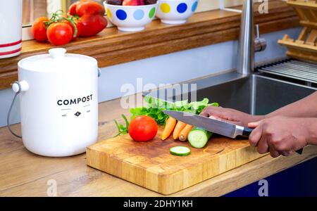 Gros plan des mains préparant des légumes dans la cuisine à côté d'un conteneur de compost de déchets de cuisine vert dans la cuisine, recycler les déchets de nourriture de cuisine pour zéro wast Banque D'Images