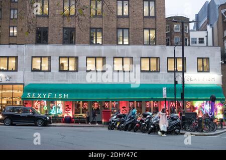 Londres, Grand Londres, Angleterre - 10 décembre 2020 : le taxi est stationné devant le magasin SexyFish, l'éclairage intérieur s'illumine le soir. Banque D'Images