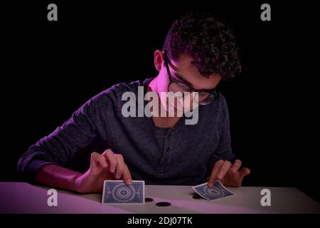 Jeune magicien caucasien adolescent, faisant un tour magique avec des cartes sur une table avec tapis. Performances en direct. Banque D'Images