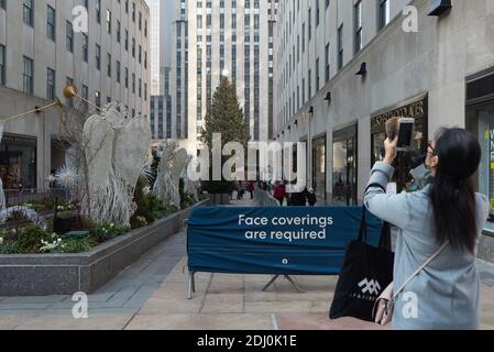 New York : un touriste portant un masque prend une photo de l'arbre de Noël du Rockefeller Center devant un panneau indiquant « une couverture du visage est requise » Banque D'Images