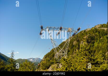 Lignes électriques et tour traversant la forêt et les montagnes contre le ciel bleu clair en Colombie-Britannique, Canada. Banque D'Images