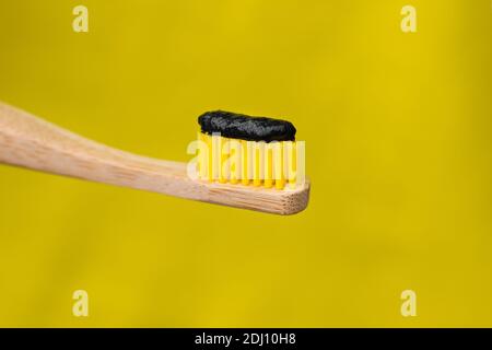 Brosse à dents écologique en bambou naturel avec dentifrice blanchissant au charbon de bois noir isolé sur fond jaune Banque D'Images