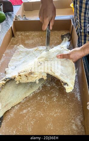 Poisson de morue séché et salé coupé en portions par un homme avec un grand couteau Banque D'Images