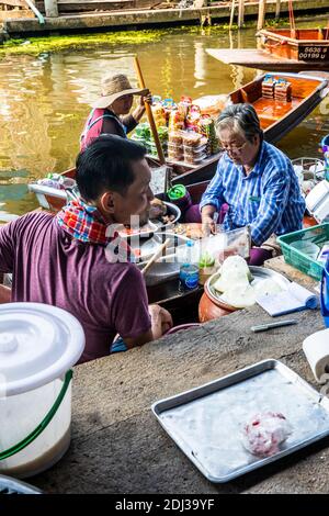 Les femmes à bord de san Pans cuisinent et servent une variété d'en-cas et de plats de rue dans le marché flottant de Damnoen près de Bangkok. Banque D'Images