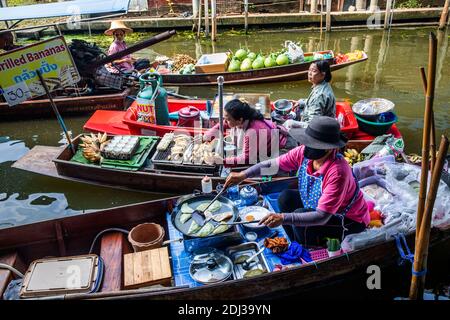 Les femmes à bord de san Pans cuisinent et servent une variété d'en-cas et de plats de rue dans le marché flottant de Damnoen près de Bangkok. Banque D'Images