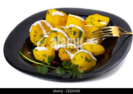 Pommes de terre cuites saupoudrées d'herbes sur une assiette noire. Banque D'Images