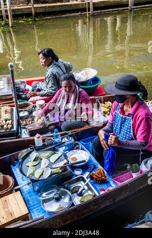 Les femmes à bord de san Pans cuisinent et servent une variété d'en-cas et de plats de rue dans le marché flottant de Damnoen près de Bangkok. Banque D'Images