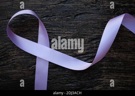 Vue de dessus du ruban couleur lavande ou orchidée violet clair sur fond de bois sombre. Sensibilisation au cancer général et testiculaire et à l'épilepsie Banque D'Images