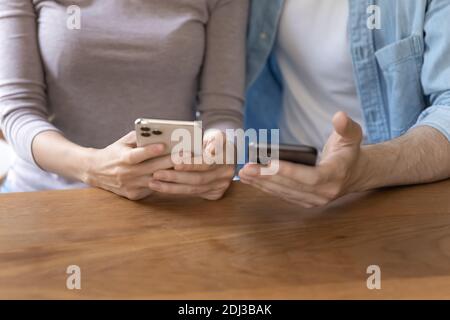 Gros plan couple utilisant un smartphone, assis à une table en bois Banque D'Images