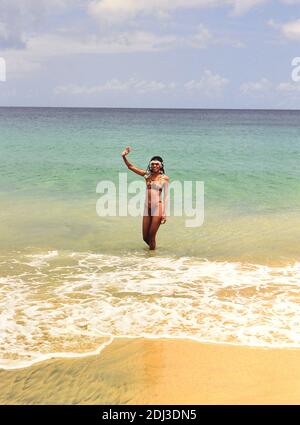 Années 1990 Trinité-et-Tobago - jeune femme locale avec des perles, des cheveux cornidés sur la plage en agitant à la caméra (Tobago, 1996) MR Banque D'Images