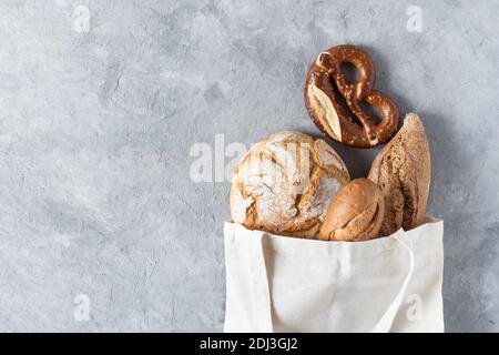 Assortiment de pains cuits au four et petits pains dans un sac de shopping en tissu blanc sur fond de béton gris vue du dessus. Pain biologique sain. Concept d'éco-shopping. Banque D'Images