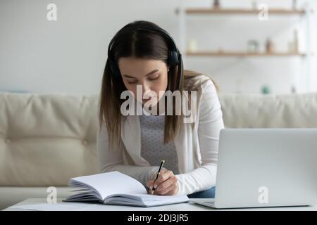 Jeune femme ciblée portant un casque à l'aide d'un ordinateur portable, écrivant des notes Banque D'Images