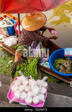 Sous la protection de son chapeau thaïlandais et d'un parapluie, une femme en. Le marché d'Amphawa travaille sur son bateau à partir duquel elle vend des produits et du riz. Banque D'Images