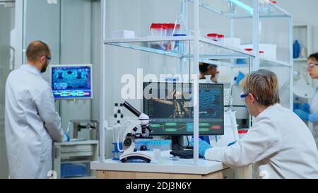 Technicien de laboratoire âgé effectuant des recherches pharmaceutiques pour les antibiotiques, traitant la maladie avec des médicaments améliorant l'ADN. Équipe multiethnique examinant l'évolution du virus à l'aide de la haute technologie pour le traitement contre le covid19 Banque D'Images