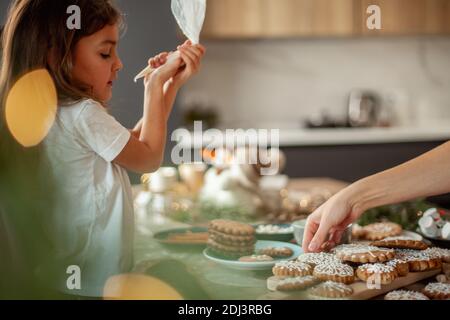 Une petite fille mignonne décore le pain d'épice avec du sucre glace. Préparation pour le concept de Noël. Banque D'Images