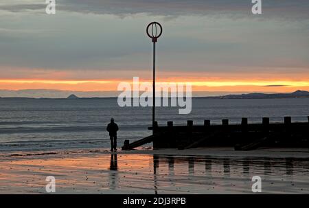 Portobello Beach, Édimbourg, Écosse, Royaume-Uni. 13 décembre 2020. Un lever de soleil nuageux au bord de la mer calme avec une température de 4 degrés centigrade.photo: Un homme solitaire regardant vers l'est Lothian au-dessus du Firth of Forth se dresse à côté de la plage grins et prend la scène tôt le matin. Crédit : Arch White/Alamy Live News. Banque D'Images