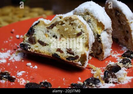 Gros plan de christstollen tranché avec des raisins secs, du sucre blanc en poudre et du massepain sur l'assiette rouge Banque D'Images