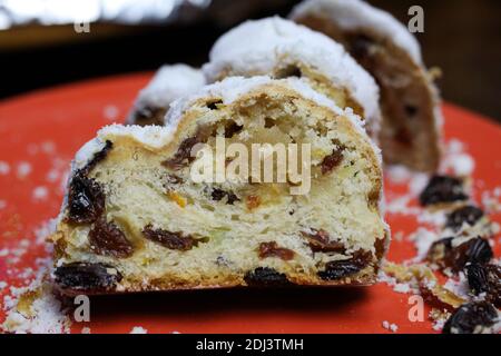 Gros plan de christstollen tranché avec des raisins secs, du sucre blanc en poudre et du massepain sur l'assiette rouge Banque D'Images