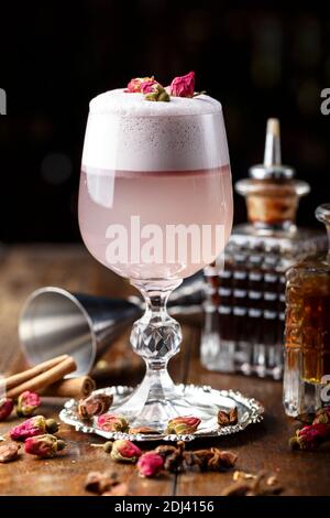 Cocktail rose femelle avec de la mousse dans un verre. décorées de rose séchée. dans l'arrière-plan est visible inventaire barman Banque D'Images