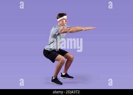 Sportif jeune gars dans les vêtements de sport faire des exercices de squats sur le lilas arrière-plan du studio Banque D'Images