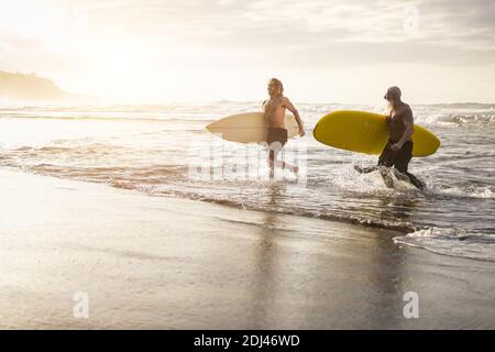 Des amis de plusieurs générations qui s'exécutent le long de la plage avec des planches de surf sur l'île plage - Focus sur les visages Banque D'Images