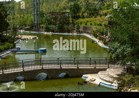 Téhéran,Iran,juillet 07,2020:Pont de pierre avec des rampes en bois, de l'autre côté de la rivière avec des oiseaux rares flottants dans le parc 'World of Birds' et les rives couvertes W Banque D'Images