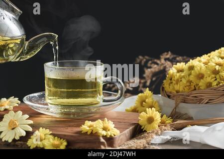Verser le thé chaud au Chrysanthemum avec de la vapeur chaude et la fleur de Chrysanthemum dans un panier sur fond noir. Beverrage sain pour boire. Herbes et médecine co Banque D'Images