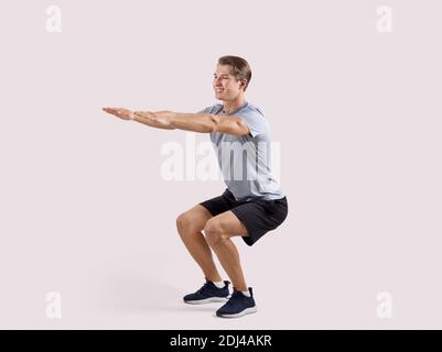 Portrait complet d'un jeune homme sportif en tenue de sport faire des squats profonds sur un arrière-plan studio léger Banque D'Images