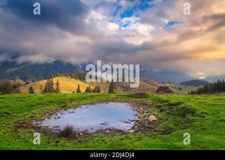 Magnifique paysage de campagne brumeux avec petit lac et montagnes brumeuses Piatra Craiului au lever du soleil, village de Pestera, Transylvanie, Roumanie, Europe Banque D'Images