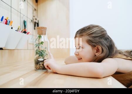 Une petite fille mignonne regarde la croissance de la plante dans un bol en verre fermé Banque D'Images