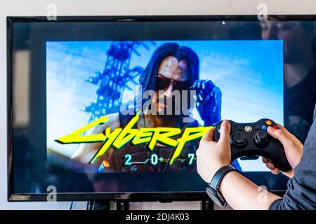 Femme tenant une manette xbox et jouant à un jeu vidéo populaire Cyber-punk 2077 sur un téléviseur et un PC Banque D'Images