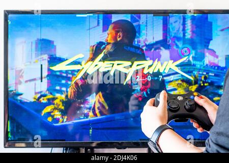 Femme tenant une manette xbox et jouant à un jeu vidéo populaire Cyber-punk 2077 sur un téléviseur et un PC Banque D'Images