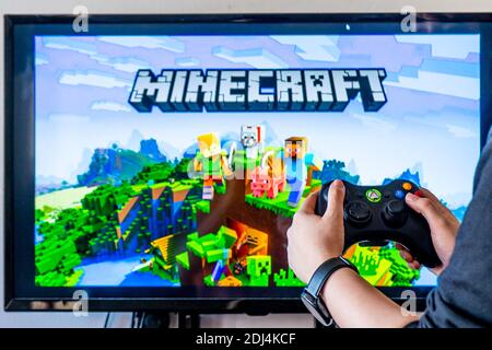 Femme tenant une manette xbox et jouant à un jeu vidéo populaire minecraft sur un téléviseur et un PC Banque D'Images