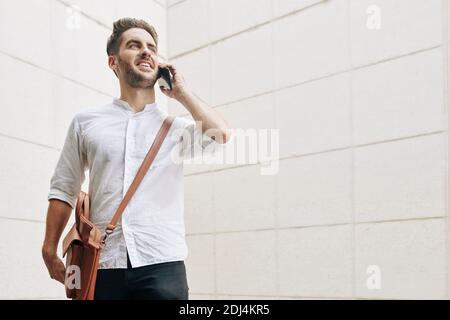 Beau fier jeune homme en chemise blanche debout à l'extérieur et parler au téléphone Banque D'Images